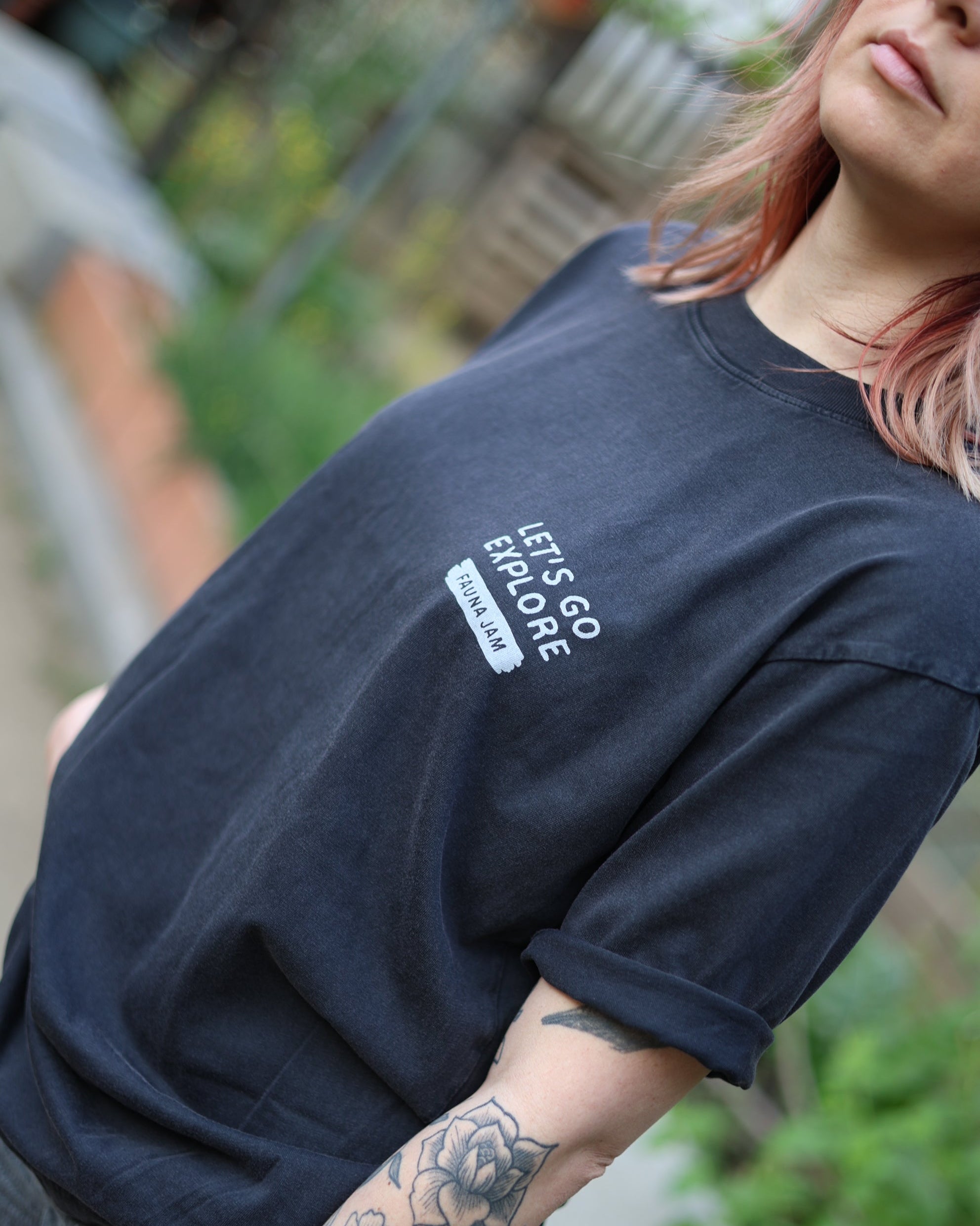 Person wearing a black t-shirt with 'Let's Go Explore' text, standing outdoors.