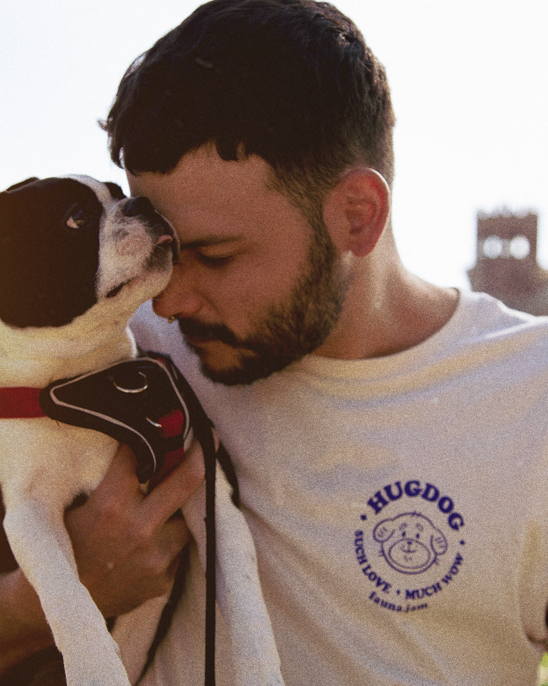 Man wearing a 'HUGDOG' shirt hugging a dog outdoors.